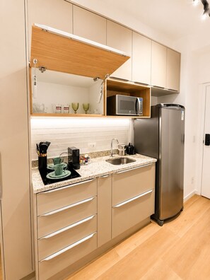 A modern kitchen with a built-in microwave, a stainless steel refrigerator, and a wooden shelf above the sink. - SETIN 1412 (São Paulo)