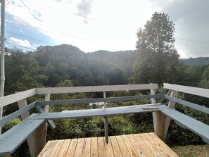 Una terraza de madera con baranda blanca que da a una ladera boscosa.