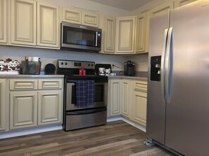 Una cocina con armarios blancos, un refrigerador de acero inoxidable, un microondas y un horno.
