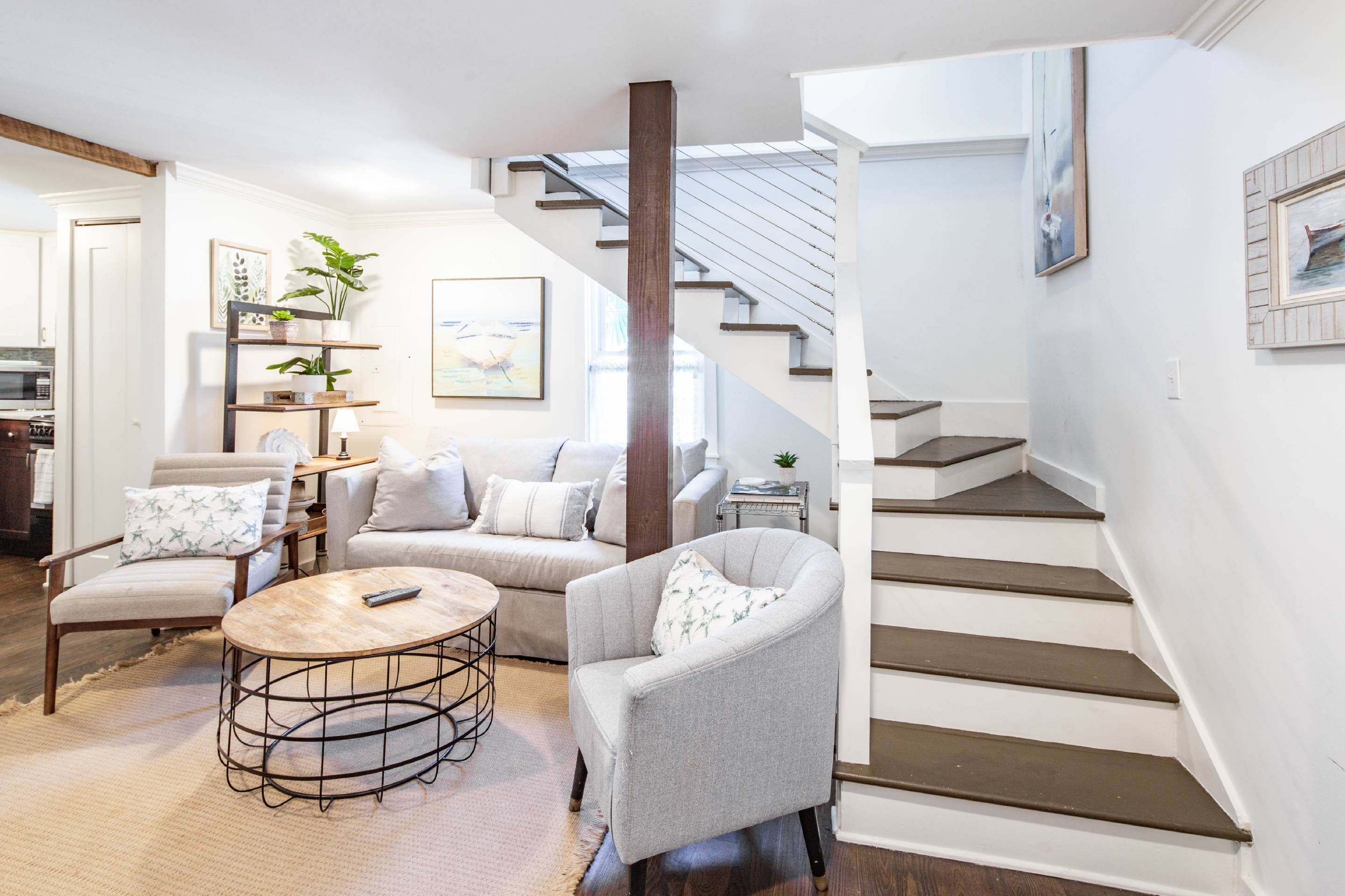 Un salon moderne avec un escalier, un coin repas et une cuisine en arrière-plan.