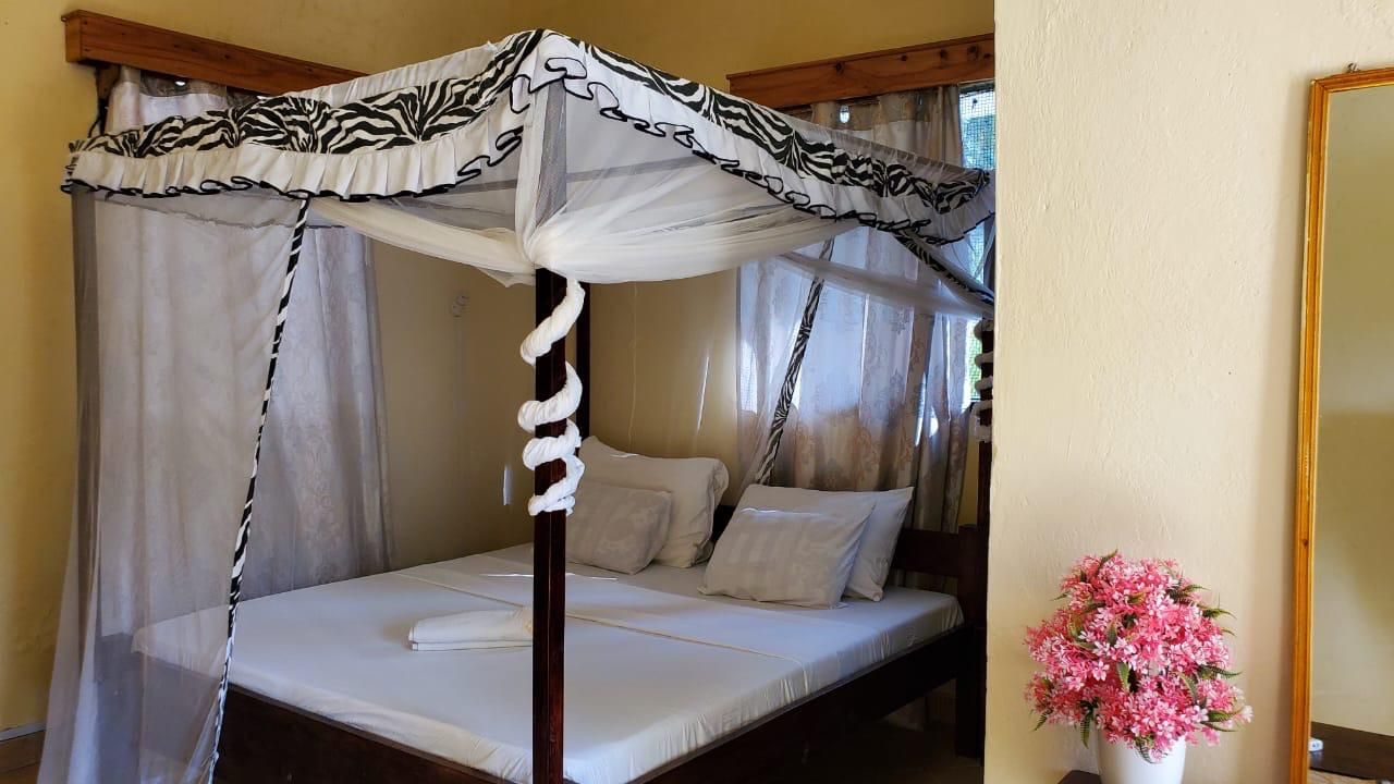 A four-poster canopy bed with white linens and a floral vase on the nightstand.