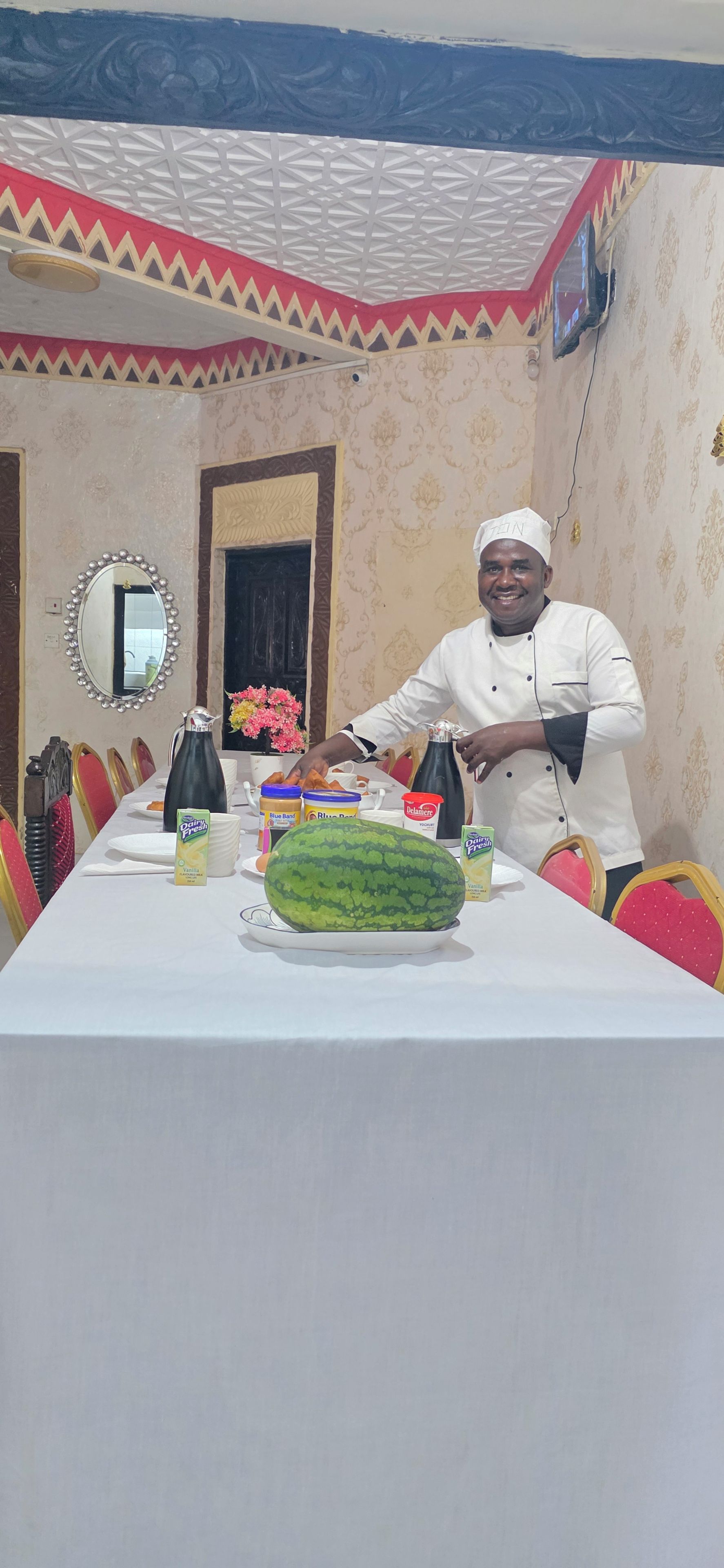 A dining table with food items and a watermelon centerpiece, surrounded by chairs.