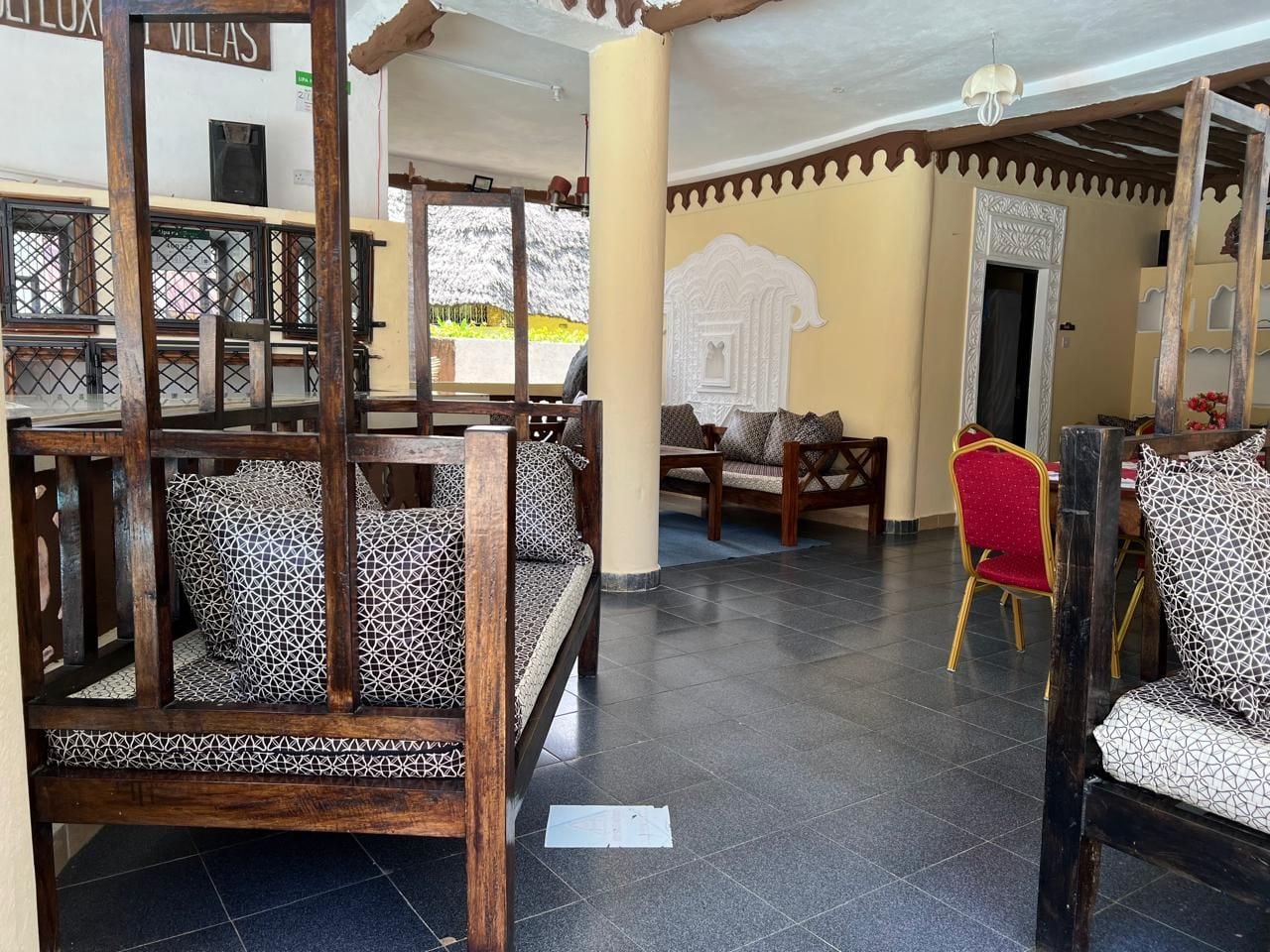 A spacious indoor area with wooden furniture, including a bench and chairs, and a tiled floor.
