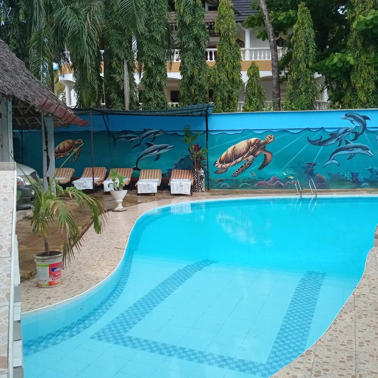 A swimming pool with a mural of sea turtles and dolphins, lounge chairs, and a palm tree.