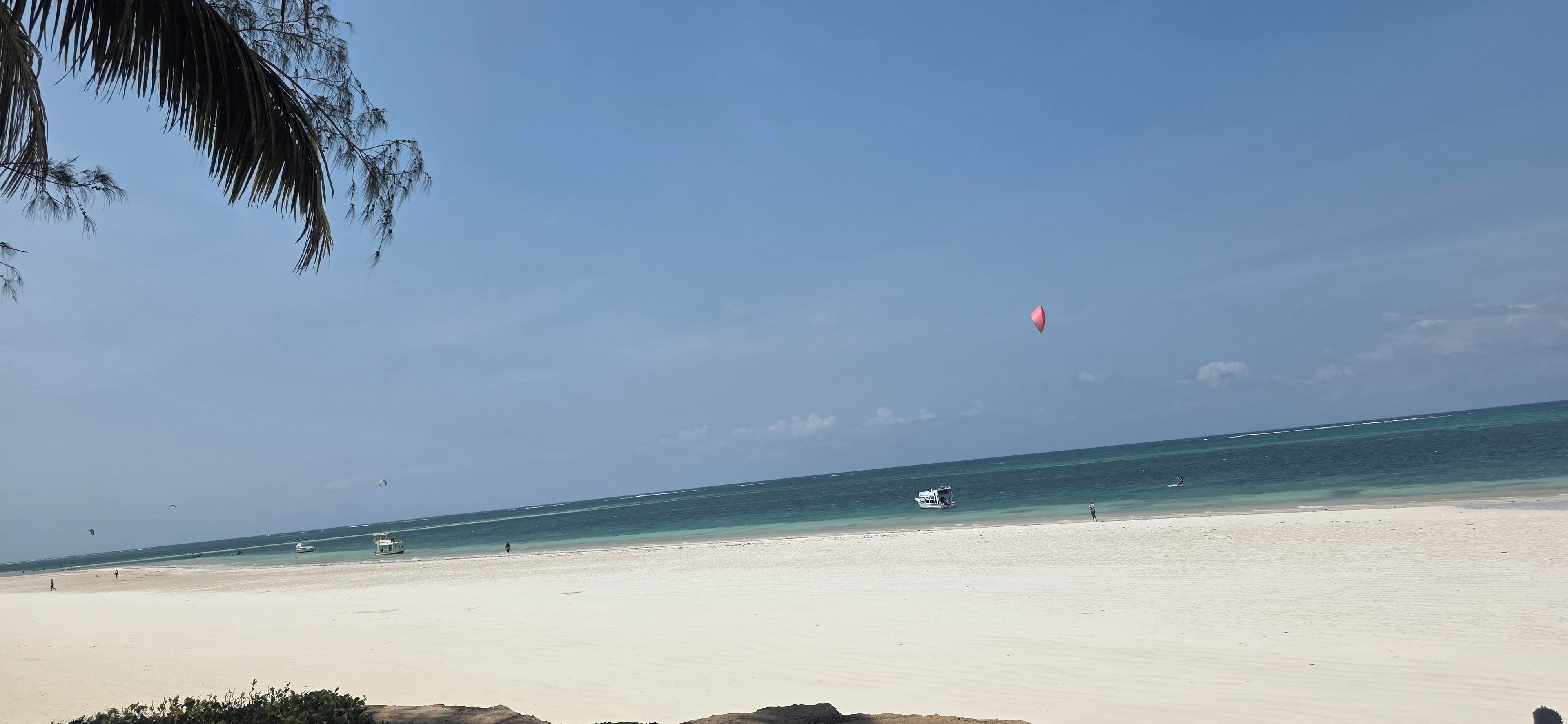 Ein Strand mit blauem Himmel, sandigem Ufer und einigen Booten im Wasser.