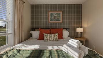 A hotel room with a bed, a nightstand with a lamp, a window with curtains, and a plaid-patterned wall.