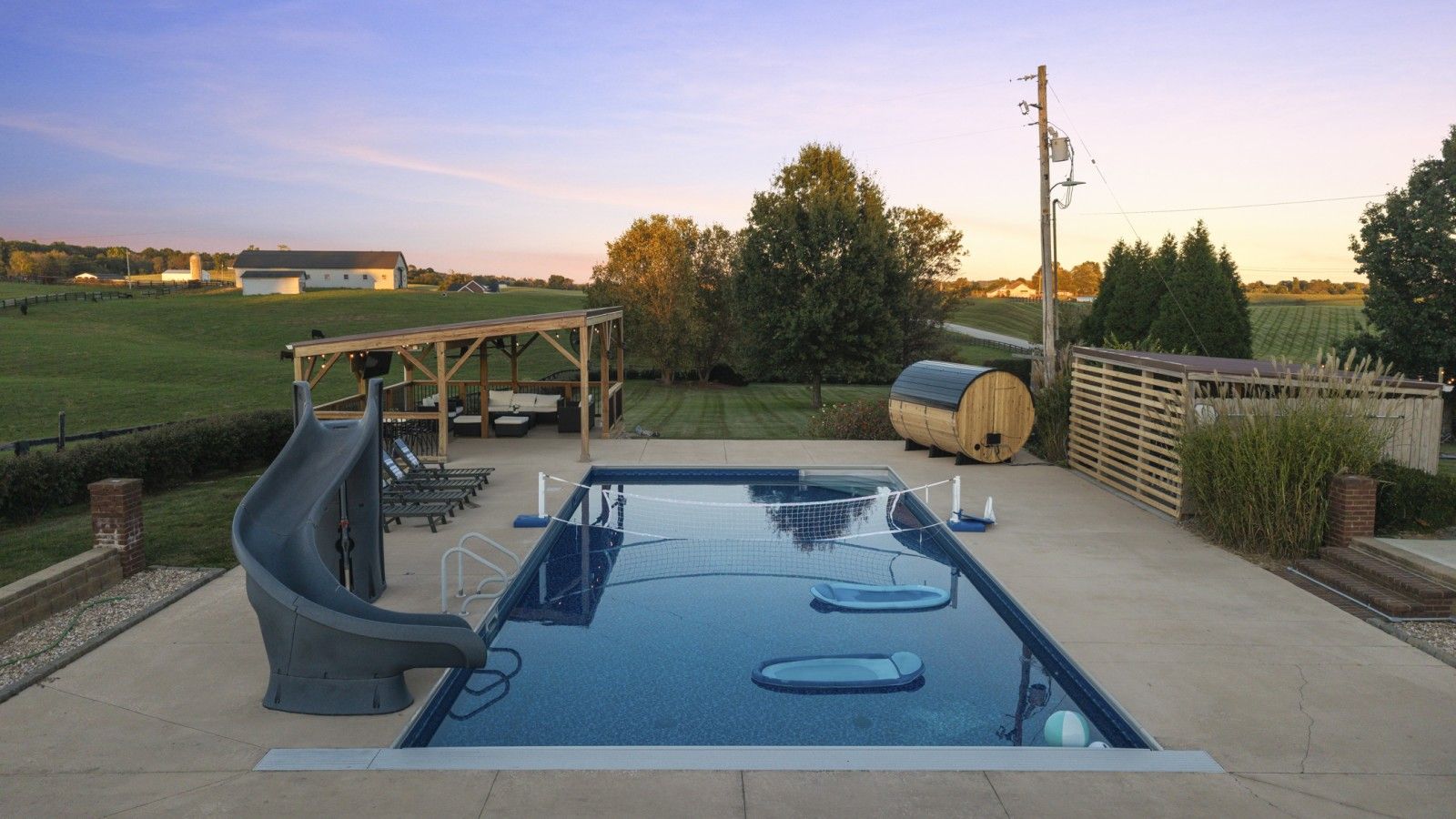 Une piscine avec un toboggan et des chaises longues, entourée d’une terrasse en bois et d’un terrain herbeux.
