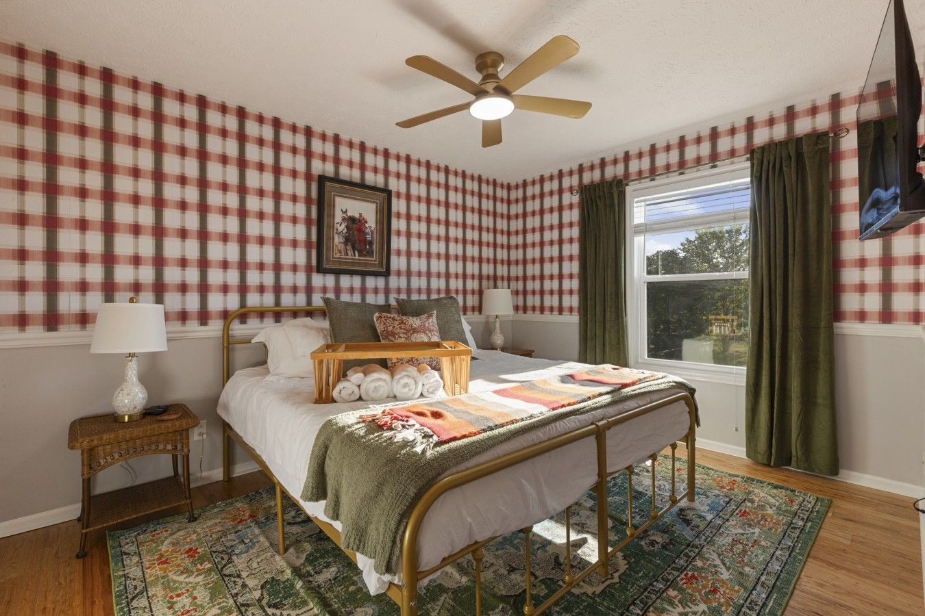 Un dormitorio con pared a cuadros, una cama con toallas dobladas, una mesita de noche con lámpara y una ventana con cortinas.