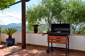 An outdoor patio with a barbecue grill, a wooden bench, a potted plant, and a view of mountains.