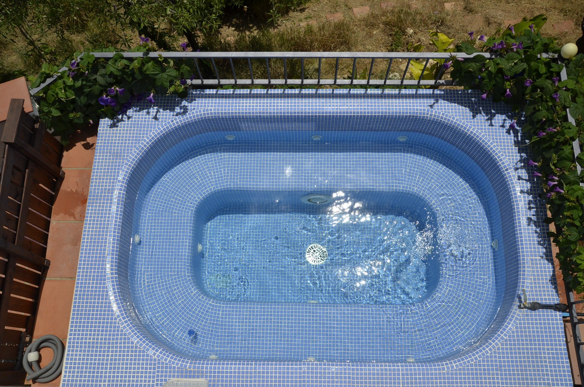 Una bañera de hidromasaje rectangular con interior de azulejos y barandilla metálica alrededor.