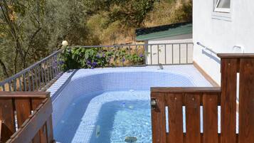 Une piscine dont le bord est recouvert de carreaux, entourée d’une terrasse en bois et d’une rambarde en métal.