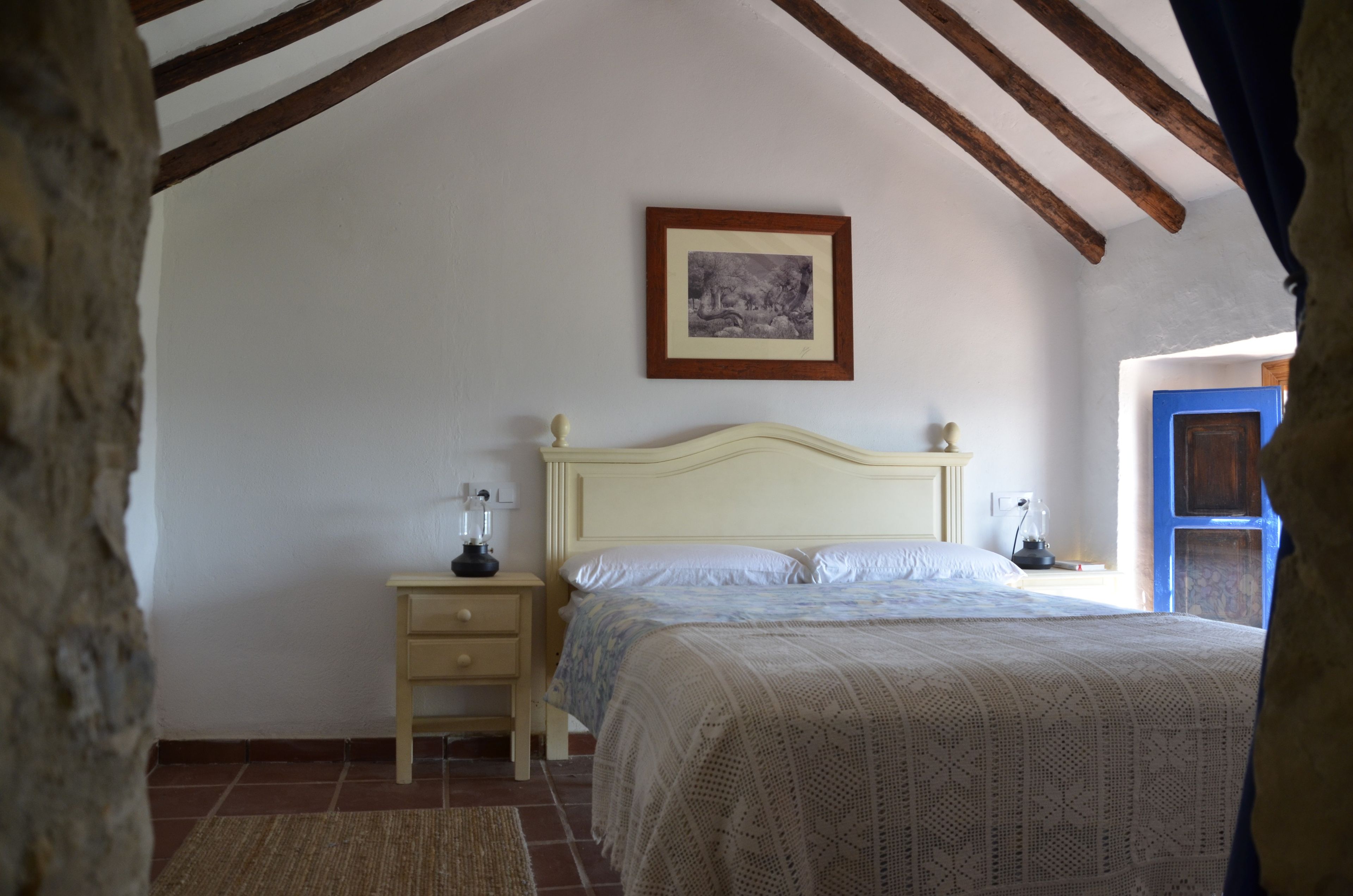 Un dormitorio con cama, mesitas de noche, un cuadro en la pared y una ventana con vistas.