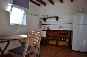 Una cuina compacta amb taula de dinar, una cadira, un armari encastrat i un frigorífic blanc.