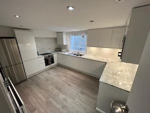 A modern kitchen with white cabinetry, a stainless steel refrigerator, a window with frosted glass, and a marble countertop. - Contemporary 4BDR Townhouse by North Laine (Brighton and Hove)
