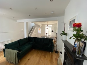 A living room with a dark green sectional sofa, a wooden floor, a fireplace, and a staircase leading to another room. - Contemporary 4BDR Townhouse by North Laine (Brighton and Hove)