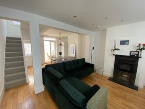 A modern living room with a dark green sectional sofa, a fireplace, and a staircase leading to another room. - Contemporary 4BDR Townhouse by North Laine (Brighton and Hove)