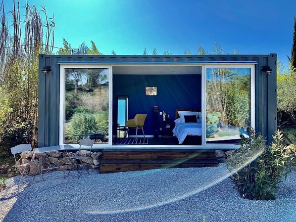Una casa moderna de vidre amb un llit, una cadira i una taula.