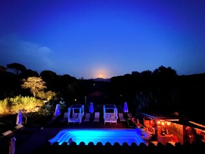 Vistall nocturn d'un complex turístic amb zona de piscina, gandules i ombrel·les.
