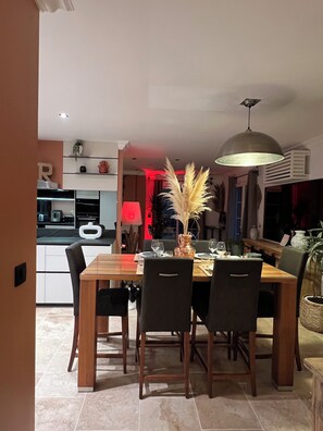 Een eethoek met een houten tafel, vier stoelen, een vaas met pampa gras en een hanglamp.