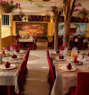 Un restaurante con varias mesas, sillas rojas y un mural tropical en la pared.