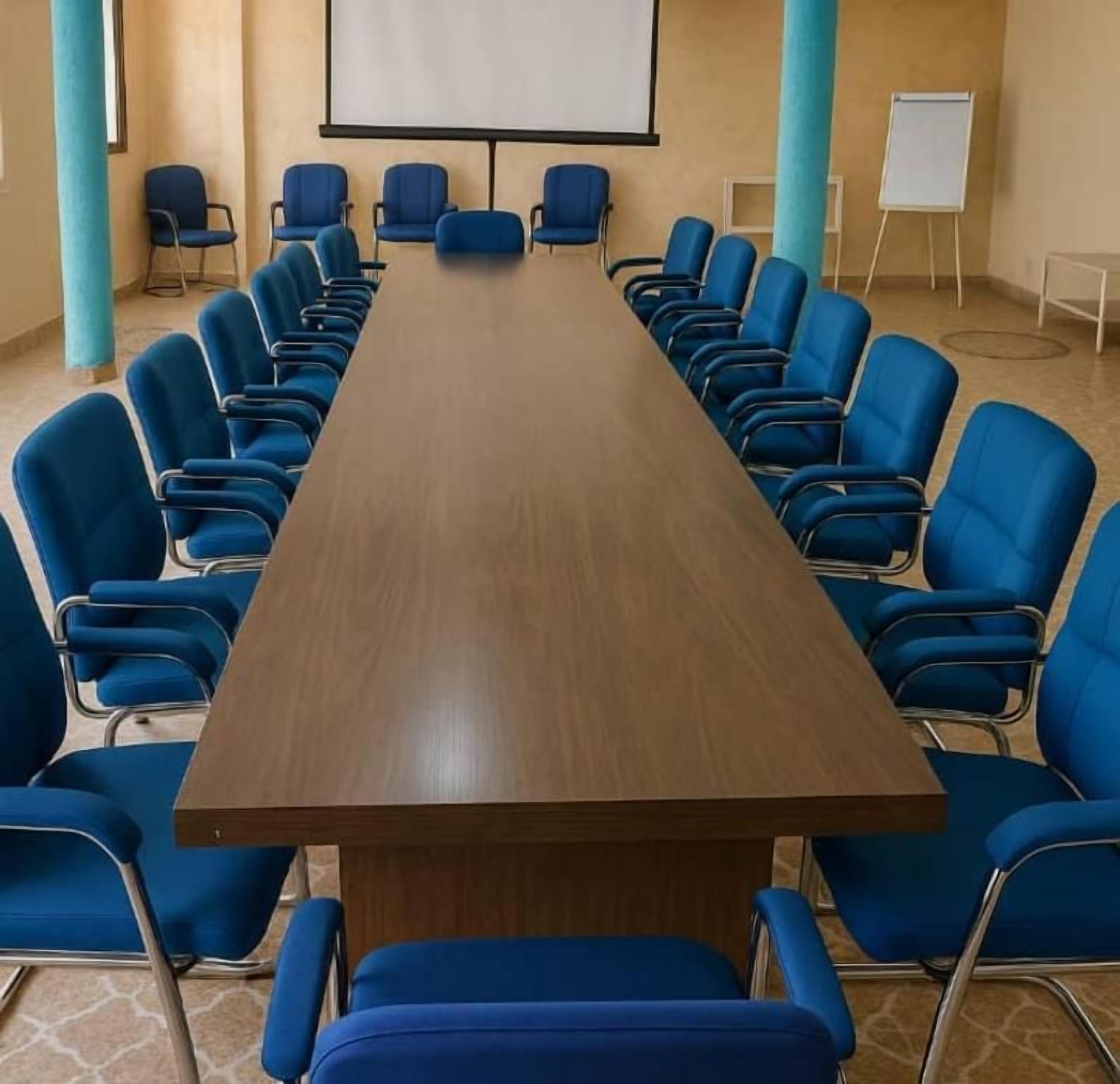A conference room with a long table and blue chairs, a whiteboard, and a projector screen.