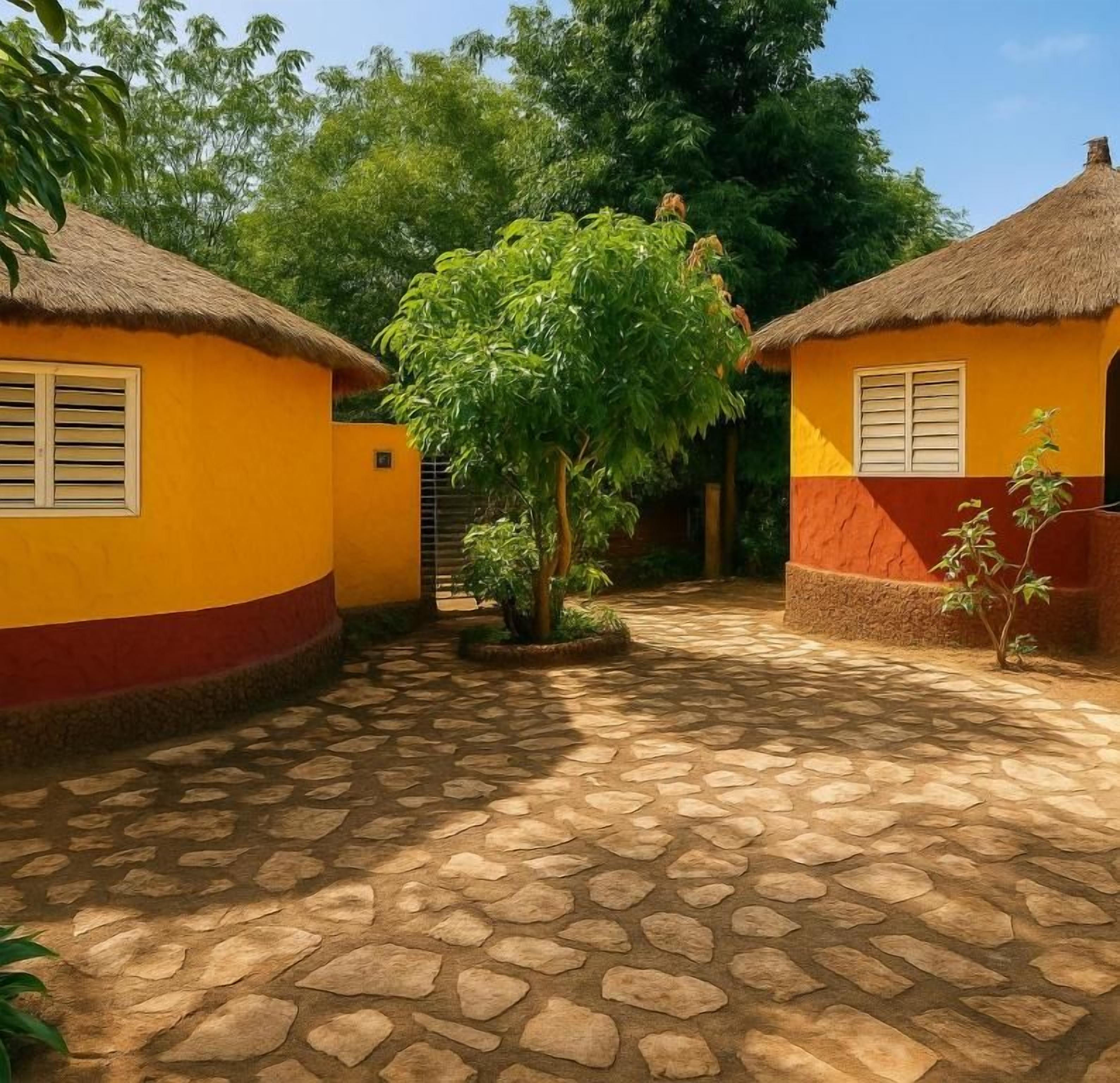 Un patio con edificios de techo de paja, un árbol en el centro y suelo empedrado.