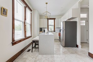 A kitchen with a central island, white cabinetry, and a stainless steel refrigerator. - Amber & Oak - Theater & Fire Pit (Omaha)