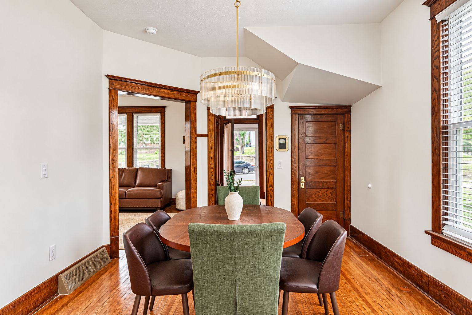 A dining room with a round table, four chairs, a chandelier, and wooden flooring.