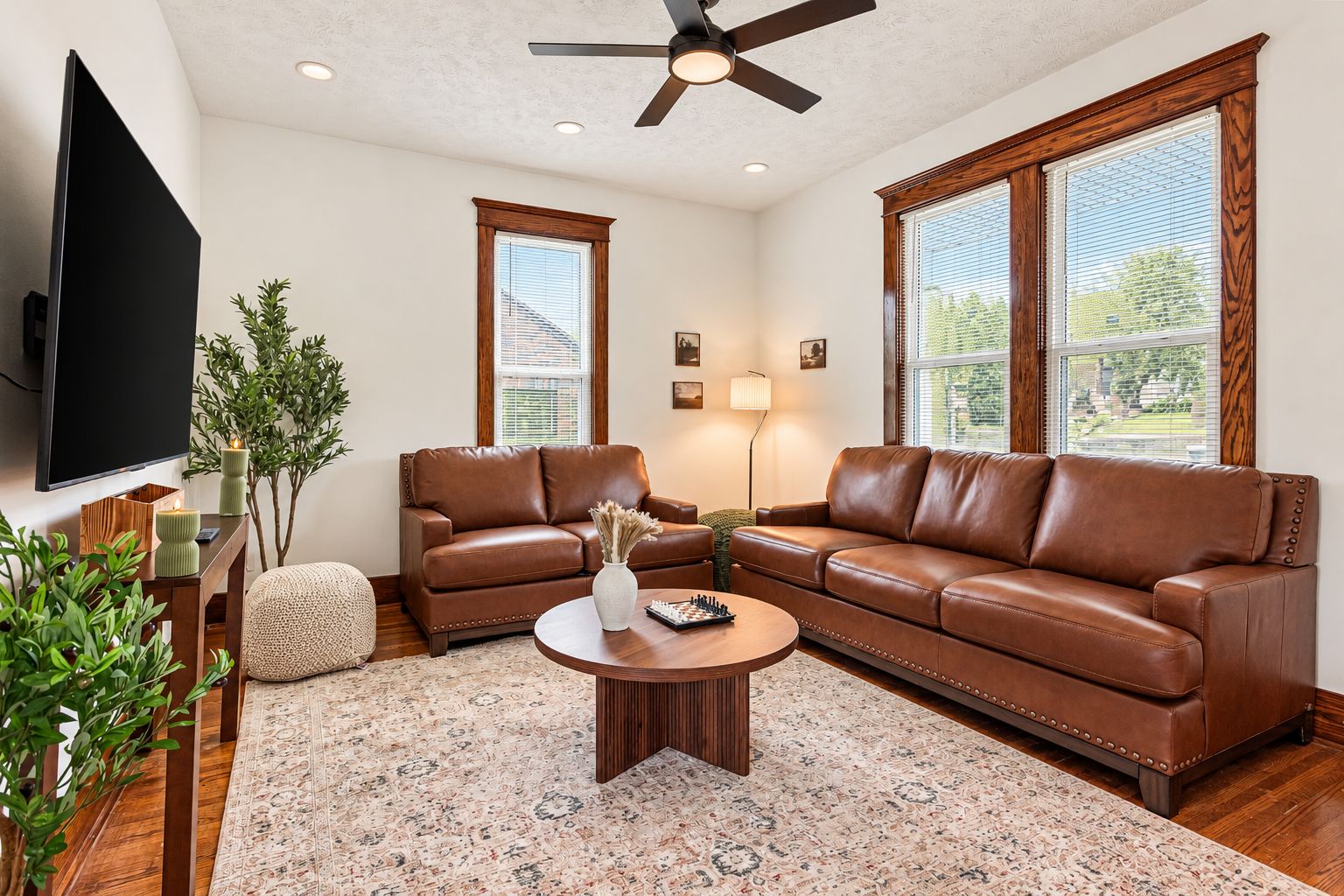 A living room with a brown leather sofa, a coffee table, a TV, and a ceiling fan.