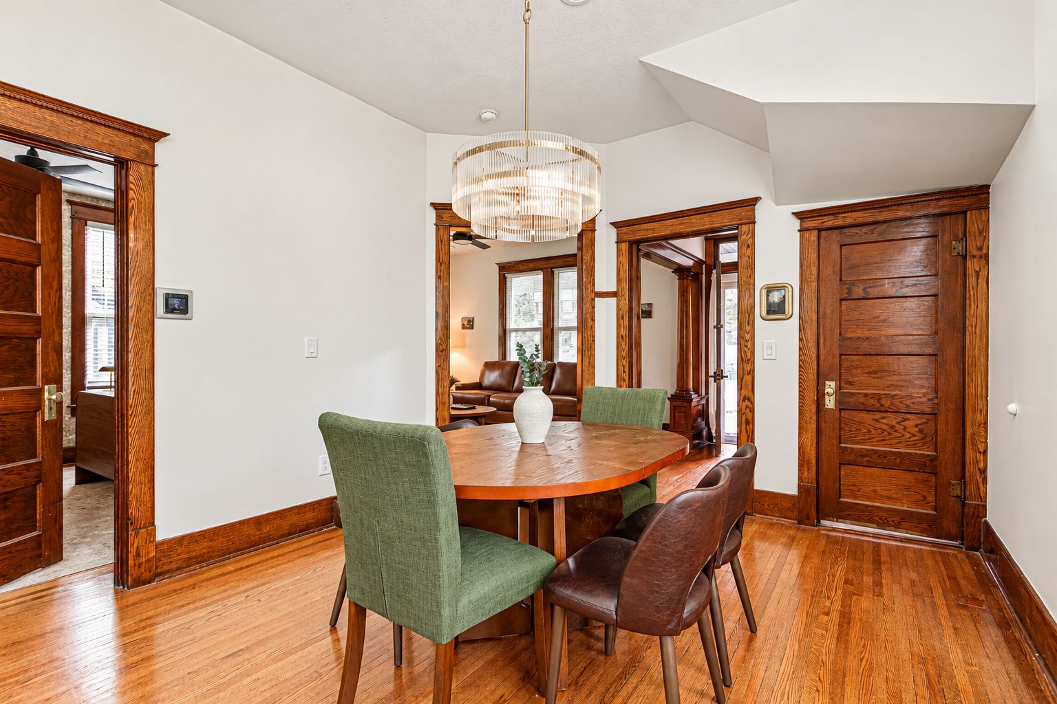 A dining room with a wooden table, green and brown upholstered chairs, a chandelier, and wooden doors.