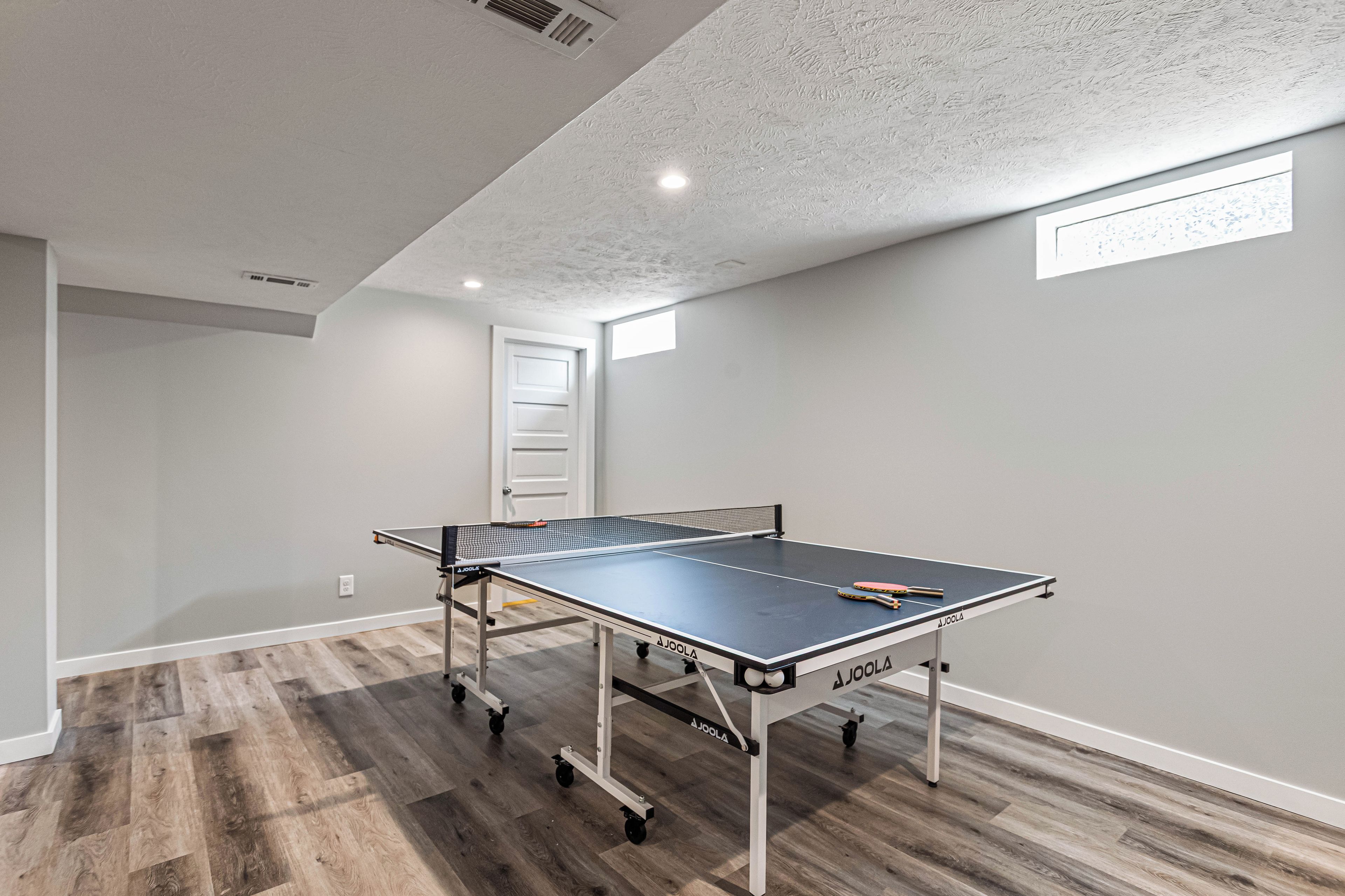 Une table de ping-pong sur roulettes, dans une pièce au plancher en bois, avec une porte blanche en arrière-plan.