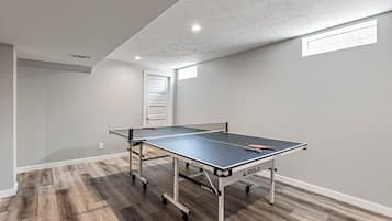 Une table de ping-pong sur roulettes, dans une pièce au plancher en bois, avec une porte blanche en arrière-plan.