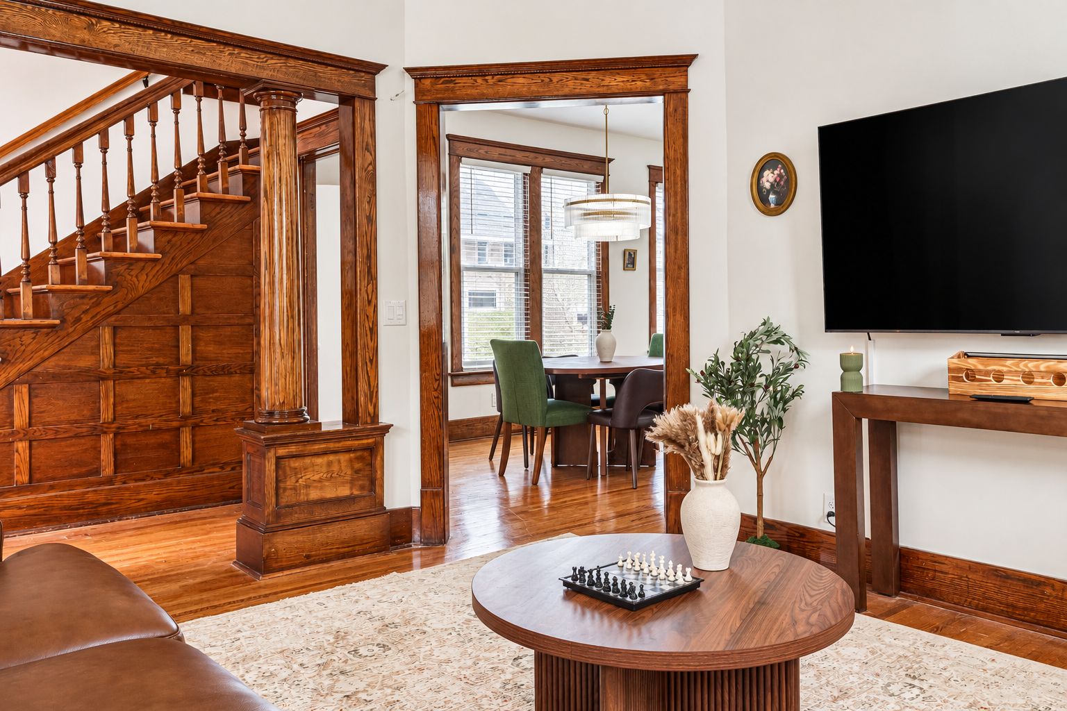 A spacious living room with a wooden staircase, a dining area, and a flat-screen TV.