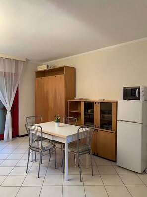 A compact kitchen with a dining table, chairs, a microwave, and a refrigerator. - Holiday Home 'Bilocale Con Terrazza E Piscina' with Air Conditioning (Marina di Bibbona)
