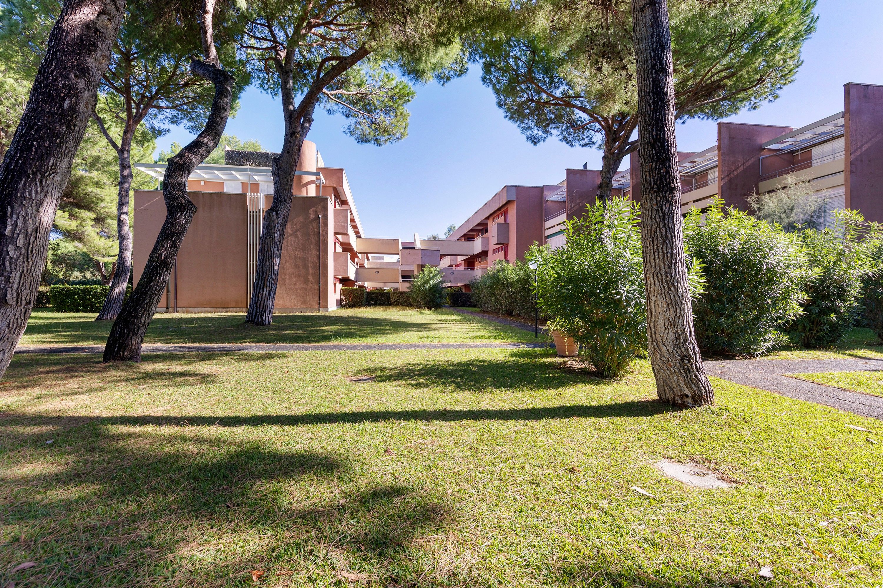 Un cortile alberato, con un vialetto e un edificio con balconi.