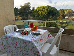 A table set outdoors with a floral tablecloth, two chairs, a basket of fruit, and a bouquet of flowers. - Holiday Home 'Monolocale Con Terrazza E Piscina' with Wi-Fi and Air Conditioning (Marina di Bibbona)