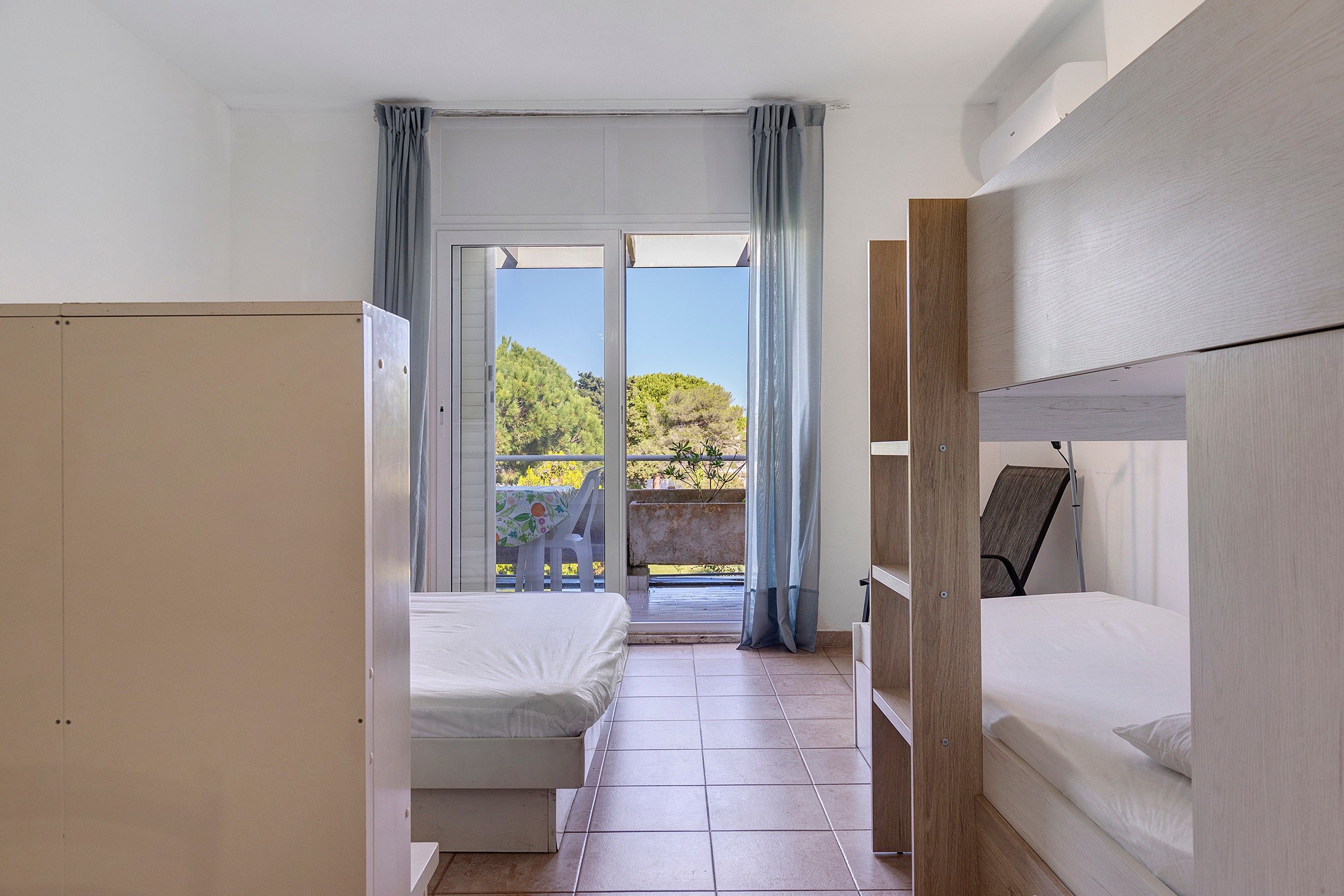 A room with two beds, a balcony, and a view of greenery.