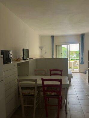 A dining area with a table, chairs, and a television. There is a window with curtains, and a view of greenery outside. - Holiday Home 'Monolocale Con Terrazza E Piscina' with Wi-Fi and Air Conditioning (Marina di Bibbona)