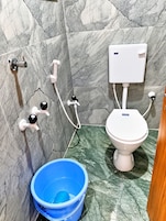 Un baño con inodoro, bidé, secador de manos y un cubo azul.