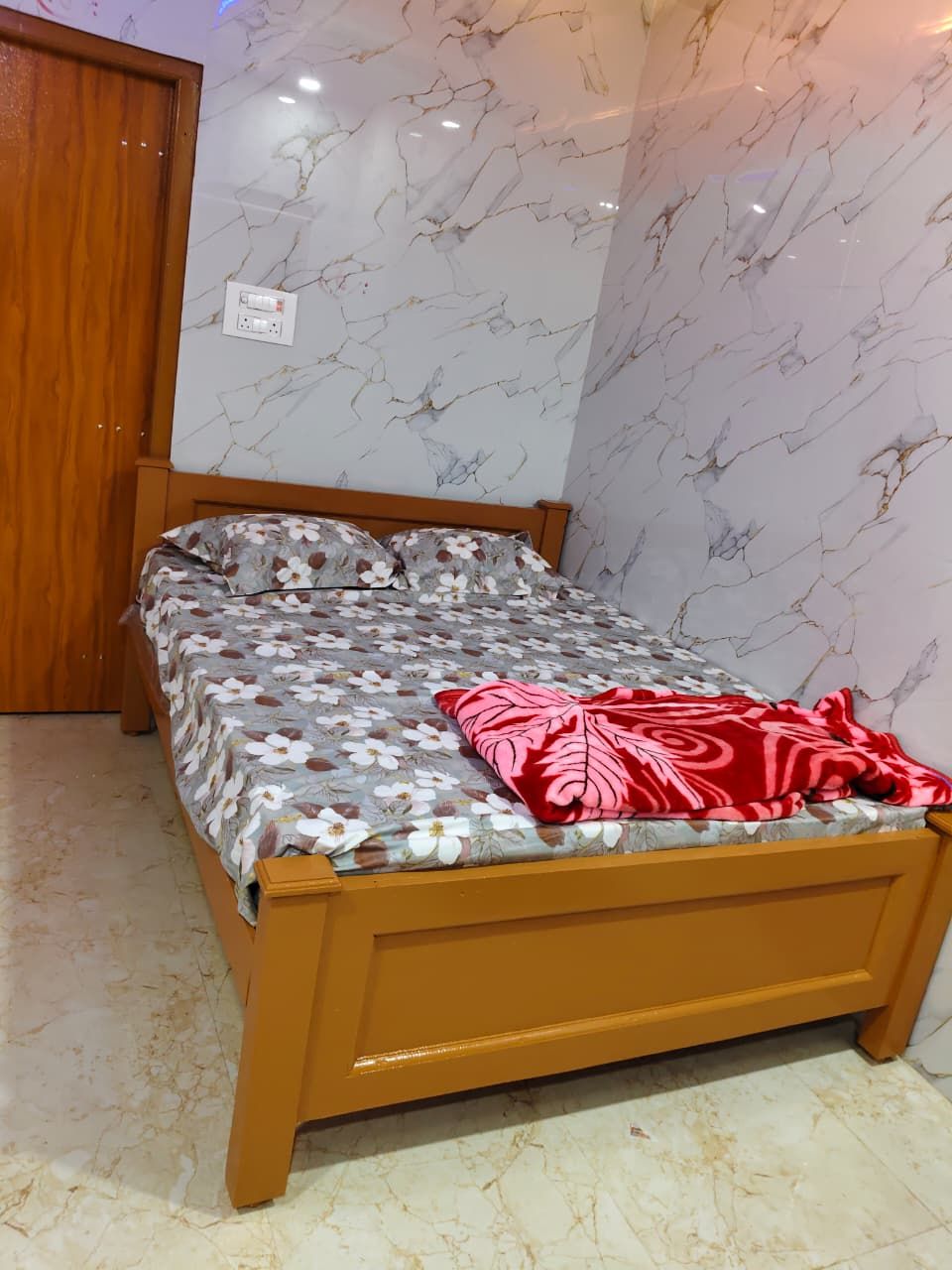 A bed with a floral bedspread, a red blanket, and a wooden headboard in a room with marble-patterned walls.