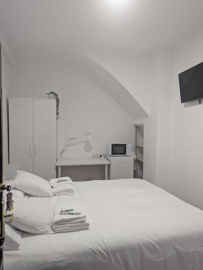 A bedroom with a bed, a desk, a TV, and a wardrobe.