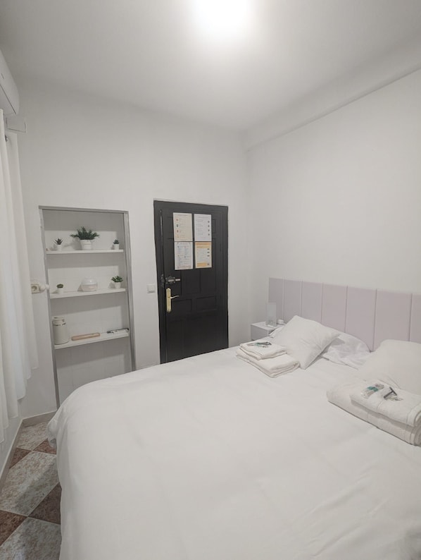 A hotel room with a bed, a wardrobe, a door with notices, and a nightstand with a lamp.
