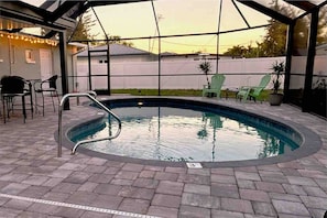 Ein Schwimmbecken mit Metallleiter, umgeben von Pflastersteinen und Gartenmöbeln.