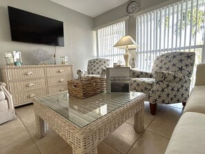 A living room with a flat-screen TV, wicker furniture, a glass coffee table, a lamp, and a 'Welcome' sign. - Free Heated Pool Home, Luxury Beds, Pet Friendly (Cape Coral)