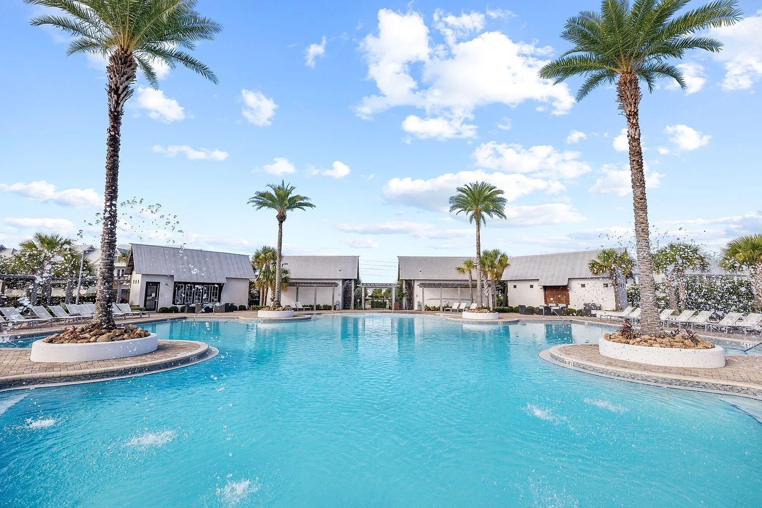 Ein Pool mit Palmen, Liegestühlen und Gebäuden im Hintergrund.