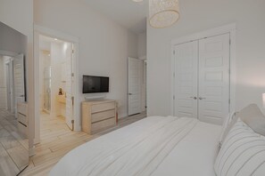 A bedroom with a bed, a television, a wardrobe, and a bathroom visible through an open door. - Luxury Stay on 30A- Gym, Bikes & Custom Golf Cart! (Inlet Beach)