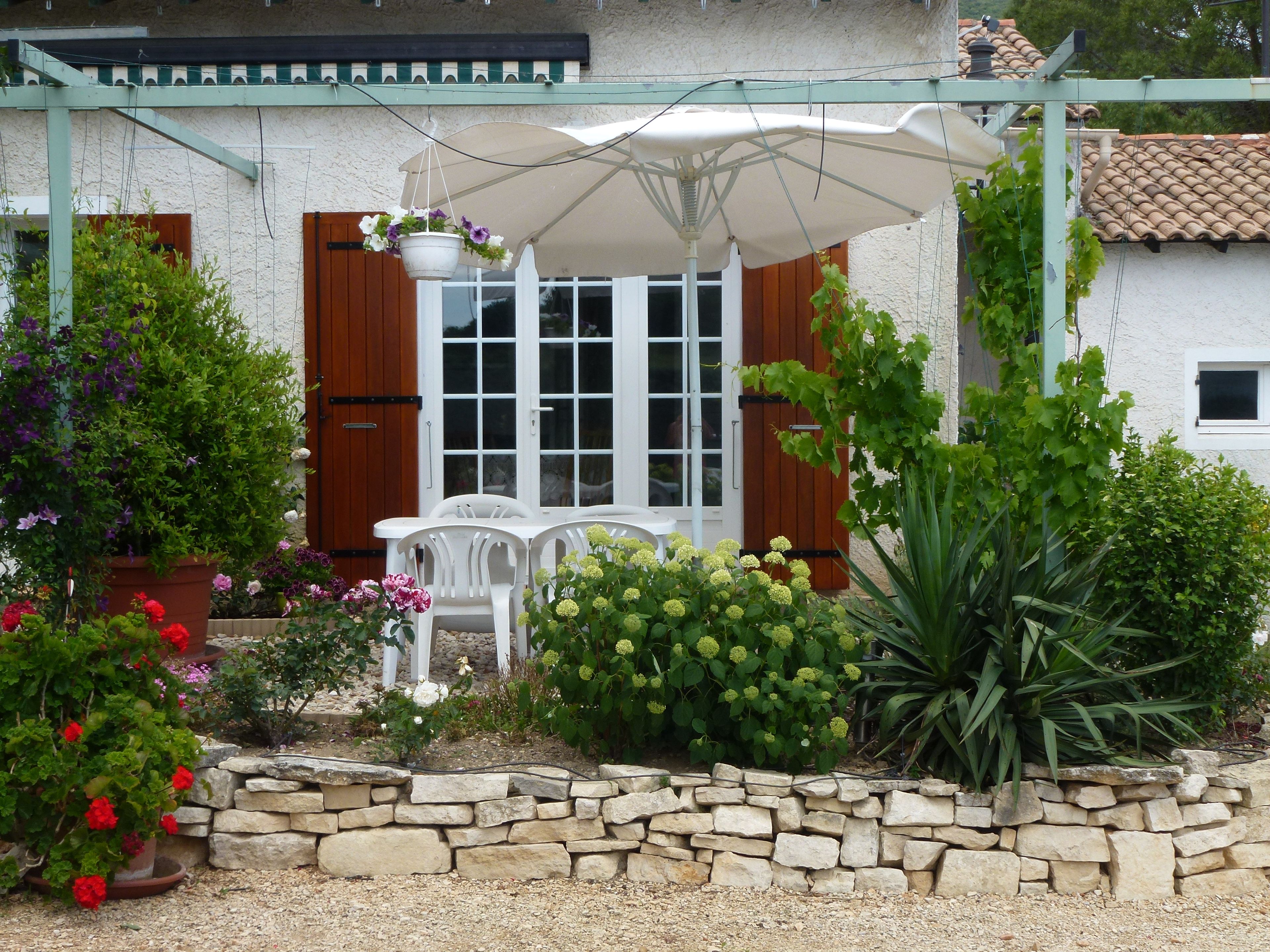 A covered patio area with a table and chairs, surrounded by a stone wall and various potted plants.