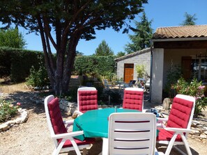 A patio with a table and chairs, a stone wall, and a building with a tiled roof. - In the heart of the Luberon Nature Park, in Rustrel: a quiet vacation rental perfect for relaxing (Rustrel)