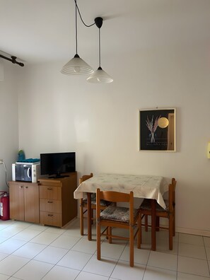 A dining area with a table, chairs, a microwave, and a television on a wooden cabinet. - Holiday Home 'Bilocale Con Terrazze' with Air Conditioning (Marina di Bibbona)