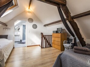 Ein Schlafzimmer mit schrägverdeckter Decke, Holzbalken, einem Bett, einer Kommode und einem Stuhl.